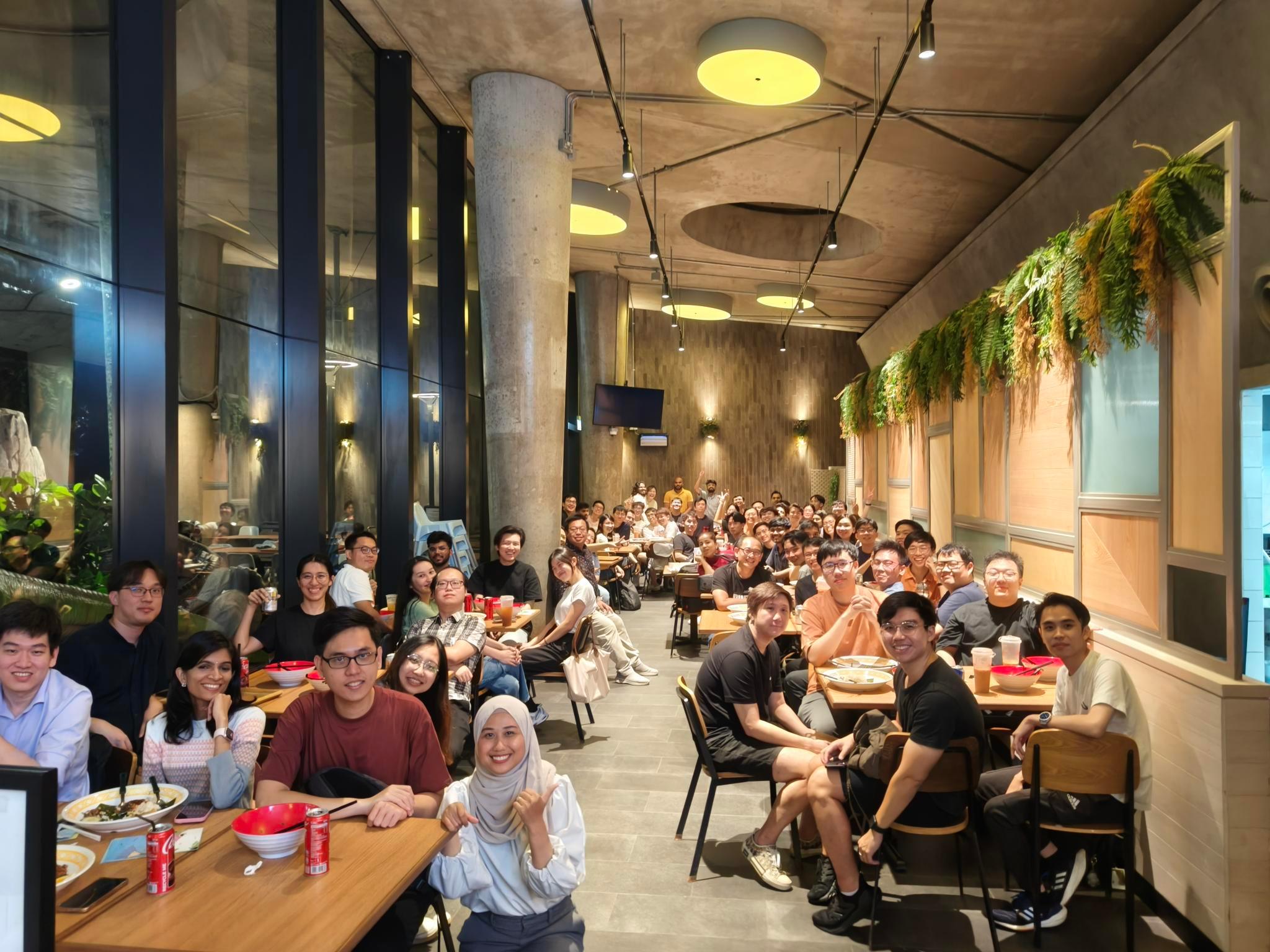 SimplifyNext team members enjoying a meal together at a restaurant, smiling and laughing while engaging in conversation. The group is diverse, employees are wearing casual attire, and the atmosphere is lively and warm.