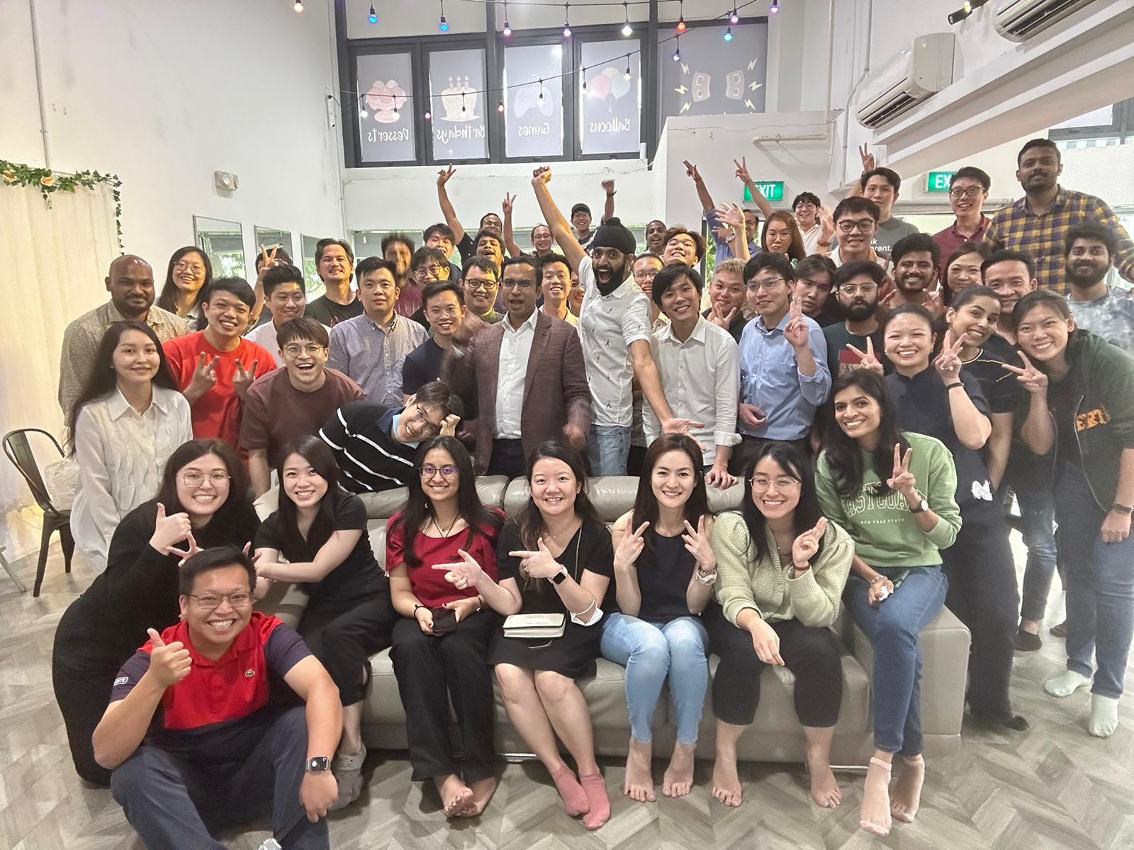 SimplifyNext Team standing together, smiling for a photo in a cozy indoor setting. Founders of SimplifyNext are in the center of the group, surrounded by team members.